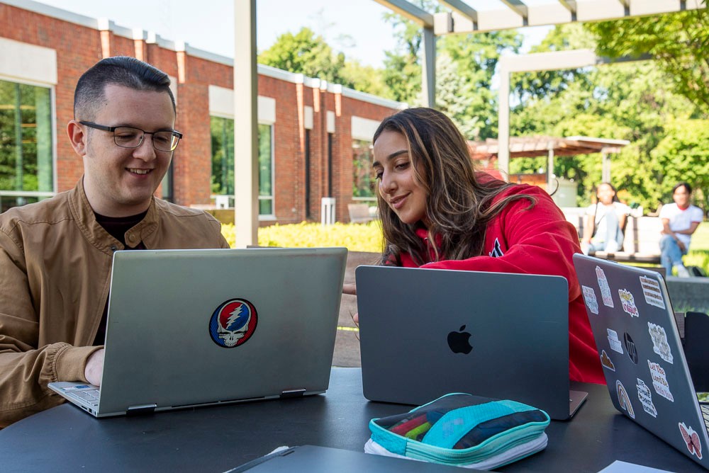 two students sitting outside at a table with a laptop