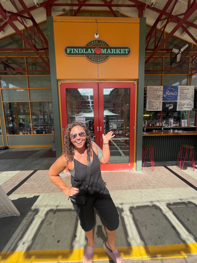woman smiling in front of Findlay Market sign